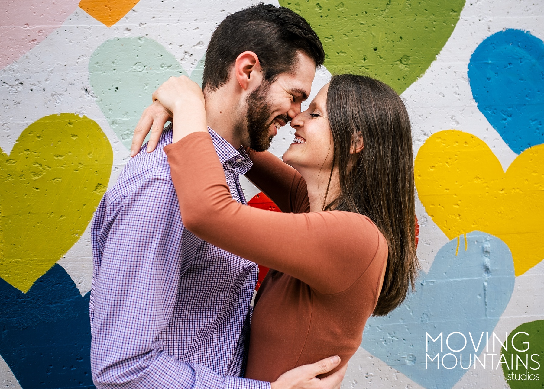 Crystal and Dylan embrace in front of the colorful heart wall in uptown charlotte